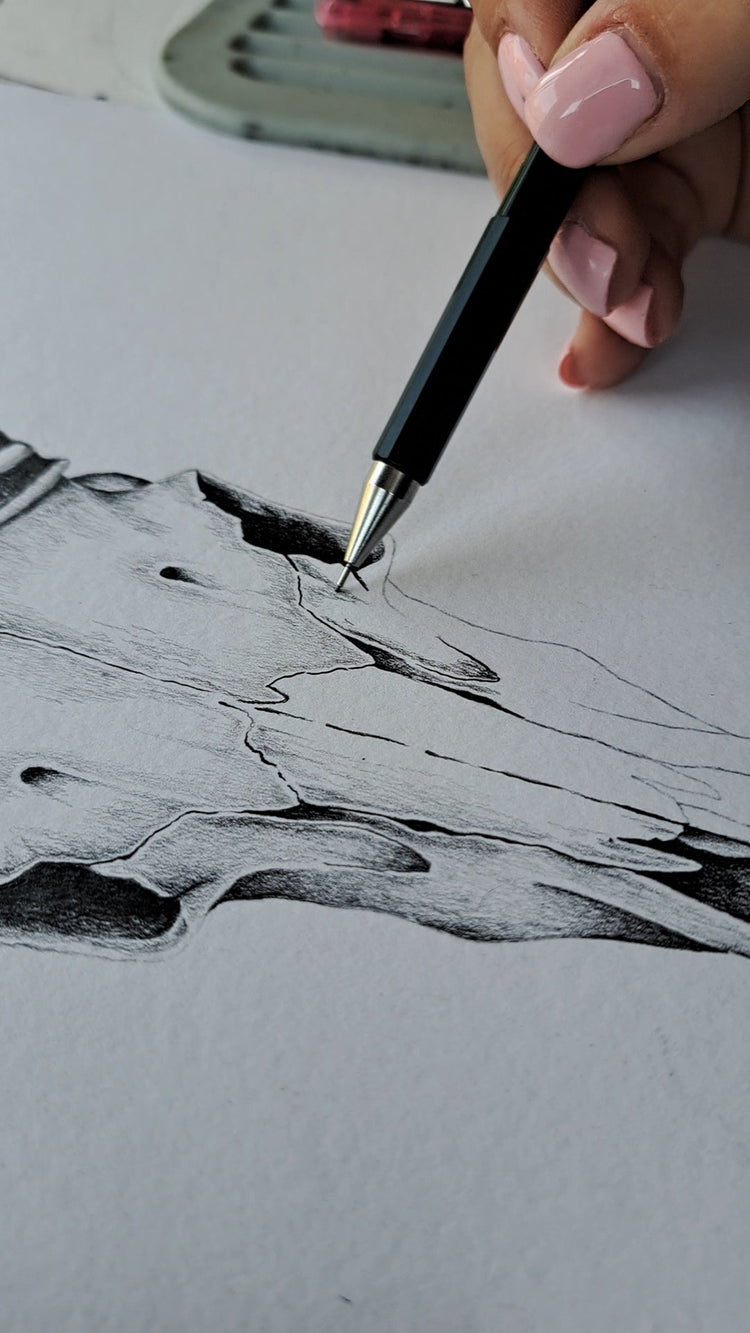 A close-up of a hand with pink manicured nails holding a black pen and drawing on white paper, creating a black and gray sketch of a textured, organic shape.